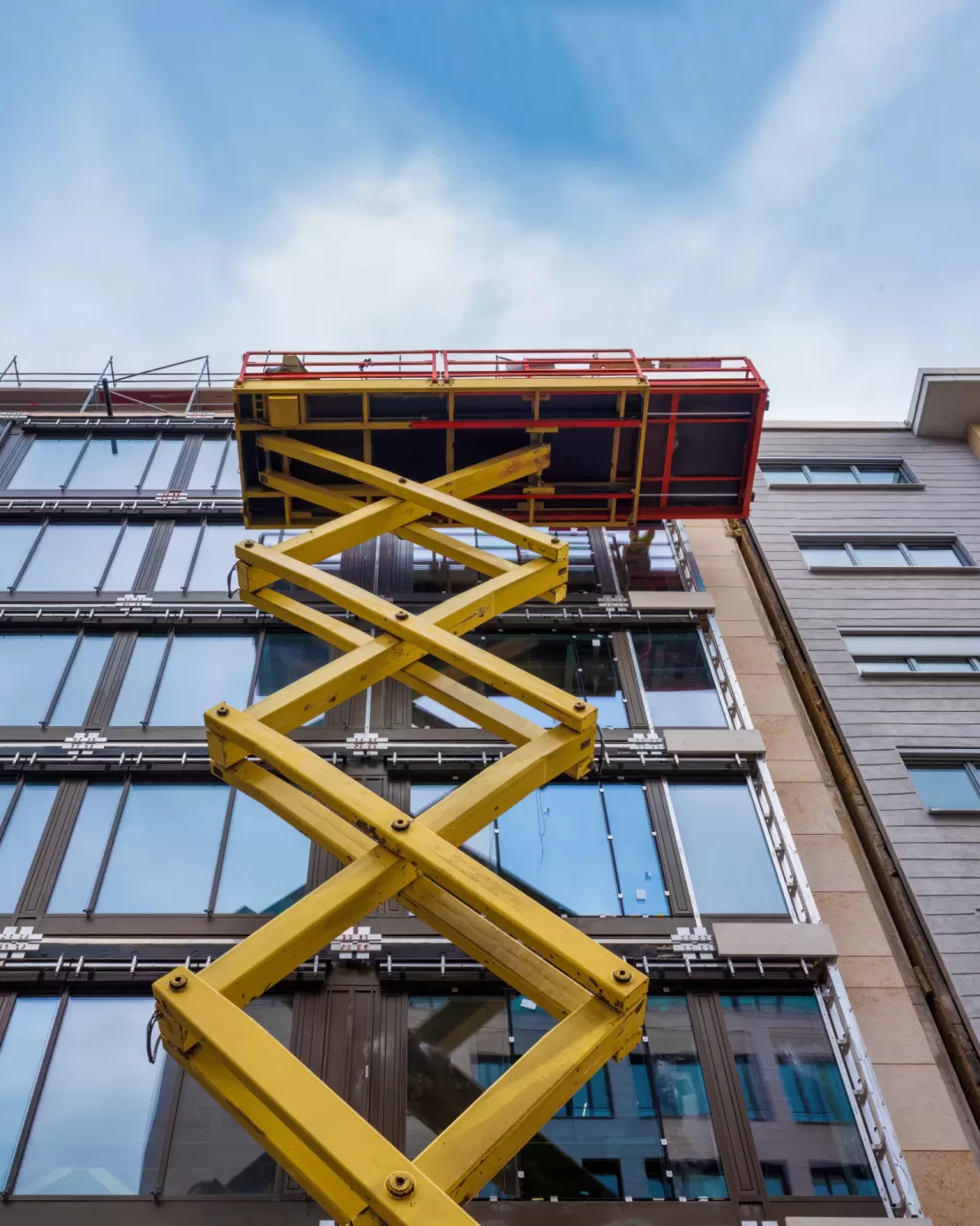 construction workers are mounting a modern building facade from an extended scissor lift. A scissor lift aerial work platform is being used to access high windows